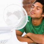 a young man stays cool with a fan as their AC is out for emergency repair